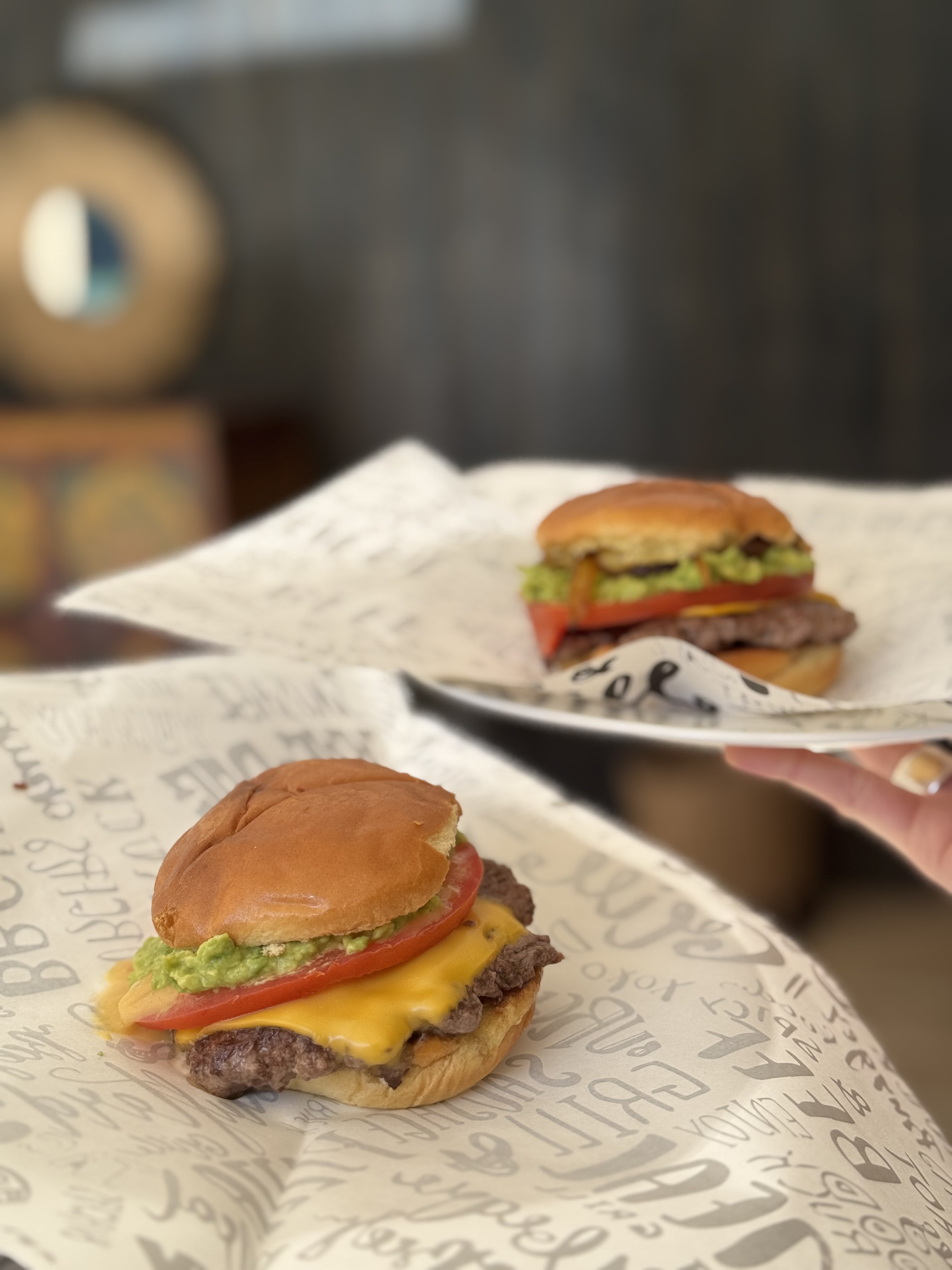 Dos hamburguesas con palta y tomate servidas en evento, mano extendiendo un plato